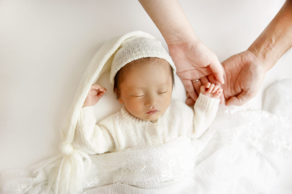 仙台のニューボーンフォト　白い背景と衣装でママやパパと手をつなぎ眠る生後10日の赤ちゃん
